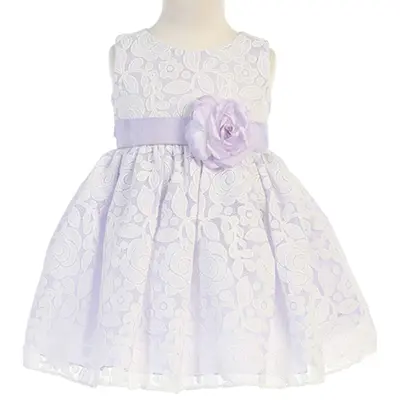 A baby girl in a white dress with purple flowers.